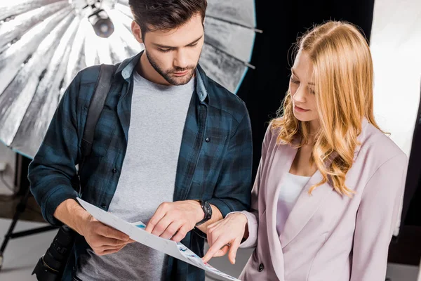 Handsome young photographer and female model looking at pictures in photo studio — Stock Photo