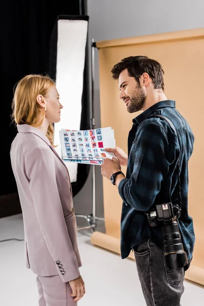 Side view of young photographer and model discussing photos and smiling each other in studio — Stock Photo