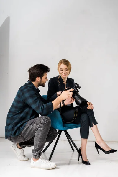 Young photographer and beautiful smiling model using photo camera together in studio — Stock Photo