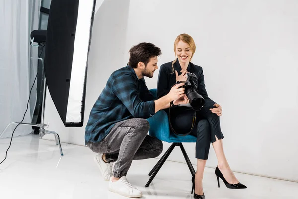 Sorrindo feliz jovem fotógrafo e bela modelo feminina usando câmera de fotos juntos em estúdio — Fotografia de Stock