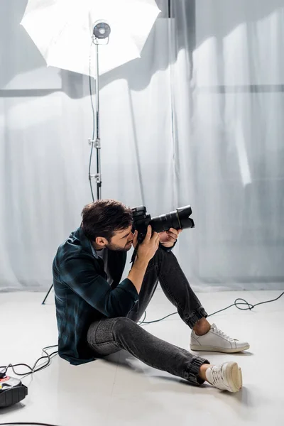 Handsome young photographer with professional camera taking pictures in studio — Stock Photo