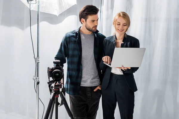 Fotograf und schöne lächelnde junge Frau mit Laptop zusammen im Fotostudio — Stockfoto