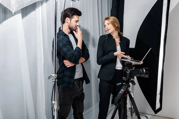 Photographe et mannequin utilisant un ordinateur portable et se souriant en studio — Photo de stock