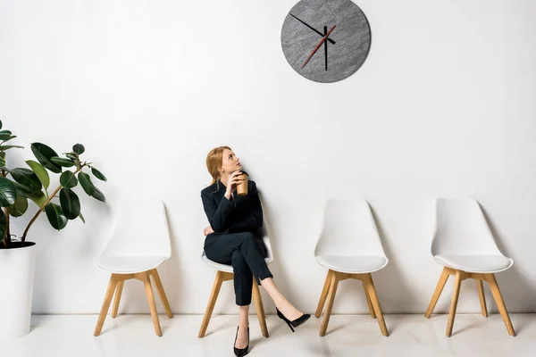 Jeune femme d'affaires tenant du café pour aller et regardant l'horloge en attendant dans la file — Photo de stock