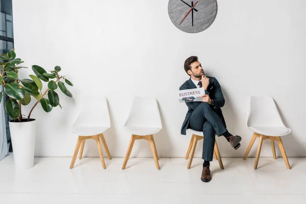 Nachdenklicher junger Geschäftsmann hält Zeitung in der Hand und wartet in der Schlange — Stockfoto