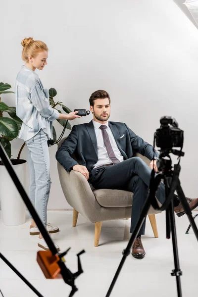 Junge Fotografin benutzt Belichtungsmesser, während sie mit einem hübschen Geschäftsmann im Studio arbeitet — Stockfoto