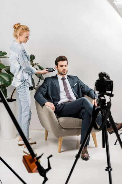 Fotógrafo joven usando medidor de luz mientras trabaja con un hombre de negocios guapo en el estudio - foto de stock