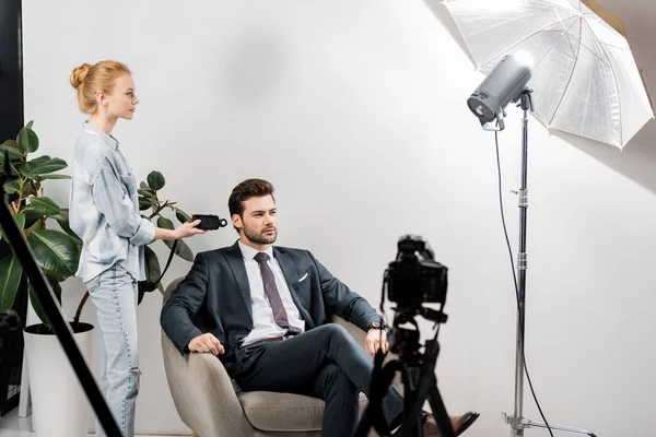 Jeune photographe utilisant compteur de lumière tout en travaillant avec beau modèle masculin en studio — Photo de stock