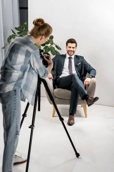 Vista posteriore di giovane fotografo scattare foto di bello uomo d'affari sorridente in ufficio — Foto stock