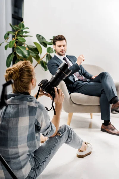 Visão traseira do fotógrafo feminino com câmera fotografar empresário bonito em estúdio — Fotografia de Stock