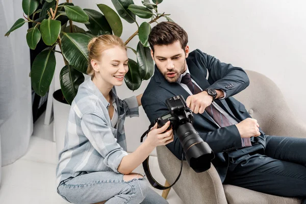 Улыбающаяся женщина фотограф и удивленный красивый бизнесмен с помощью камеры в фотостудии — стоковое фото