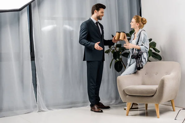 Fotógrafo sonriente y modelo sosteniendo café para ir y hablar en el estudio de fotos - foto de stock