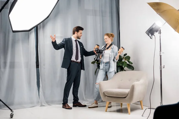 Feliz hombre de negocios sosteniendo café para ir y hablar con el fotógrafo en el estudio - foto de stock