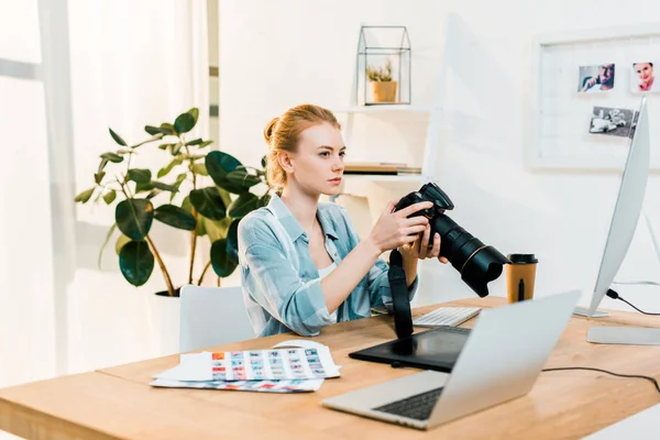 Belle jeune photographe tenant appareil photo et retoucher des photos dans le bureau — Photo de stock