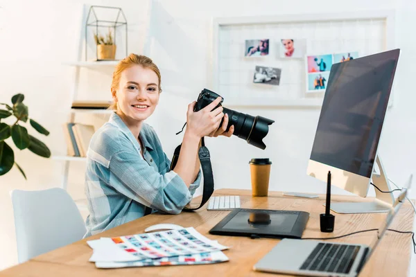 Красивая молодая женщина-фотограф улыбается перед камерой во время работы в офисе — стоковое фото