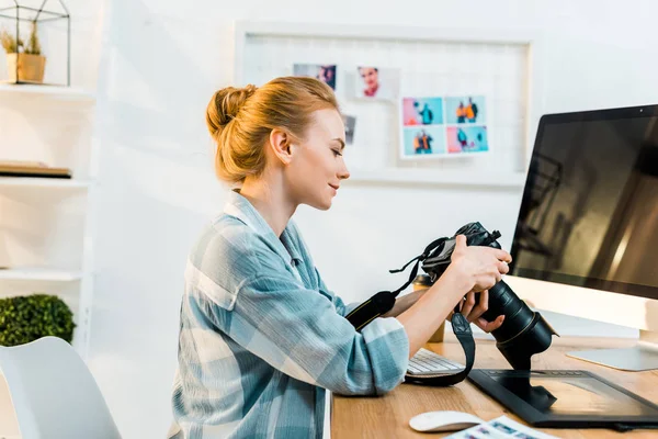 Vue latérale d'une jeune photographe souriante travaillant avec un appareil photo au bureau — Photo de stock