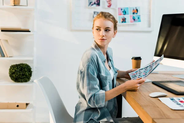 Beautiful young retoucher working with photos and looking away in office — Stock Photo