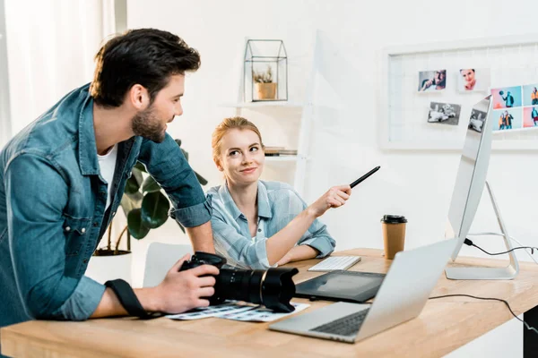 Smiling young photographers discussing and retouching photos at workplace — Stock Photo