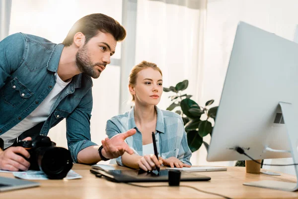 Fotógrafos jóvenes profesionales que usan dispositivos digitales y retocan fotos en el lugar de trabajo - foto de stock