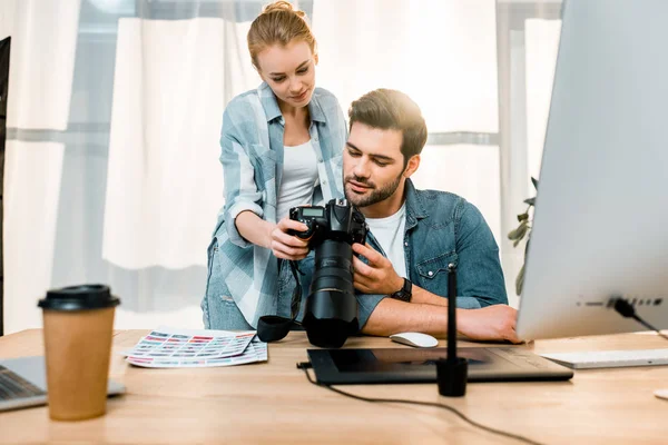 Jeunes photographes souriants professionnels utilisant un appareil photo ensemble dans le bureau — Photo de stock