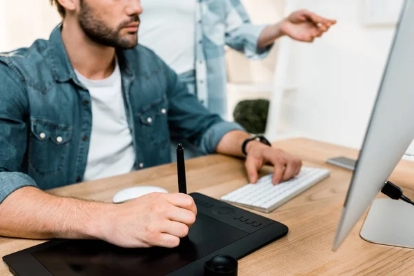 Cropped shot of male retoucher using drawing tablet while workign with colleague in office — Stock Photo