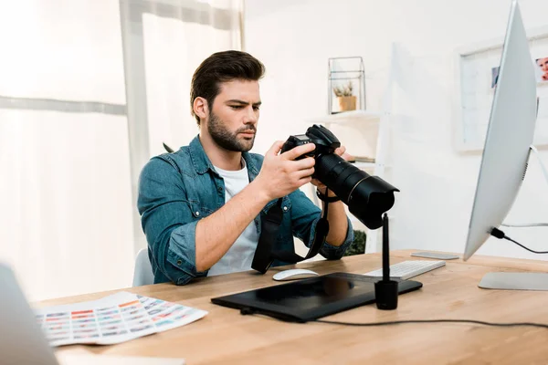 Bonito profissional jovem fotógrafo usando câmera no local de trabalho — Fotografia de Stock