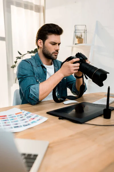 Bonito jovem fotógrafo usando câmera no local de trabalho — Fotografia de Stock