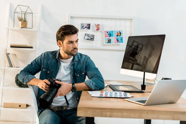 Schöner junger Fotograf mit Kamera und wegschauendem Blick im Büro — Stockfoto