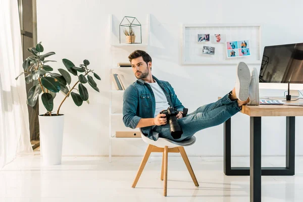 Schöner junger Fotograf mit Kamera und wegschauendem Blick im Büro — Stockfoto