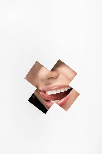 Cropped shot of young woman licking lips through cross shaped hole on white — Stock Photo