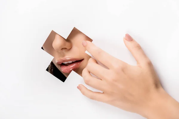 Abgeschnittene Aufnahme weiblicher Hand und Lippen durch kreuzförmiges Loch auf weiß — Stockfoto