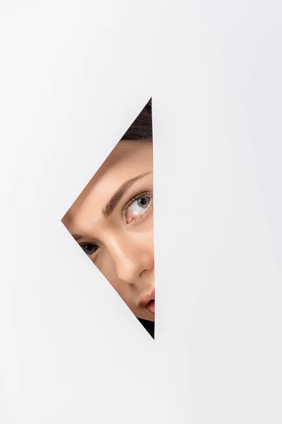 Beautiful young woman looking away through hole on white — Stock Photo