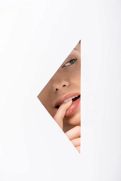 Обрізаний знімок молодої жінки кусає палець і дивиться в сторону через отвір на білому — стокове фото