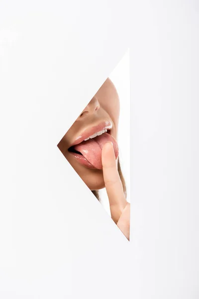 Colpo ritagliato di giovane donna leccare dito attraverso il buco sul bianco — Foto stock