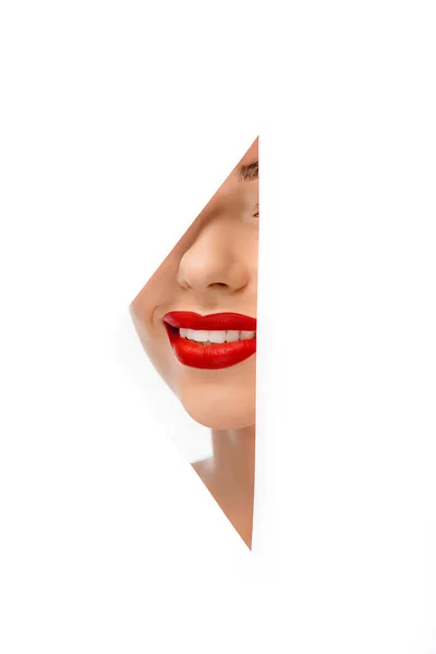 Обрезанный снимок улыбающейся молодой женщины с красными губами через отверстие на белом — стоковое фото