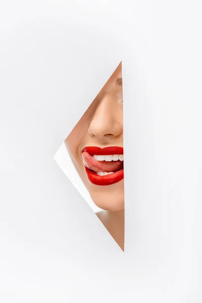 Обрізаний знімок дівчини лиже губи через отвір на білому — стокове фото