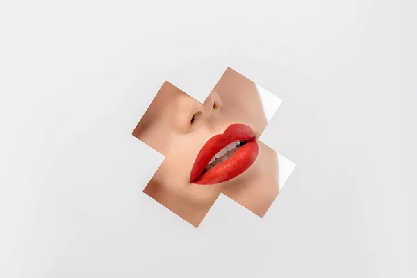 Cropped shot of young woman with red lips through cross shaped hole on white — Stock Photo