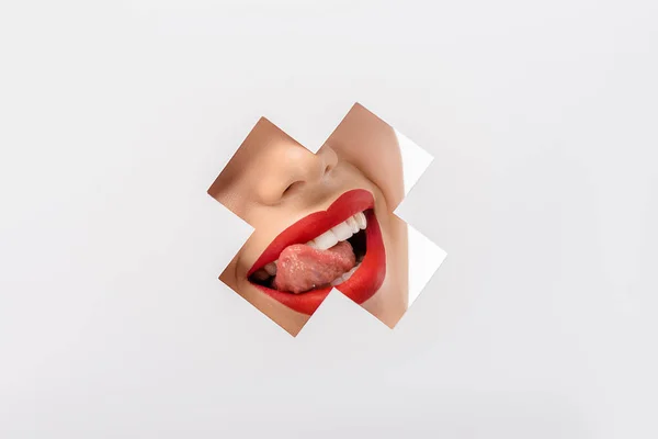 Cropped shot of girl licking lips through cross shaped hole on white — Stock Photo