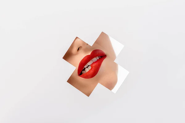 Cropped shot of girl biting red lip through cross shaped hole on white — Stock Photo