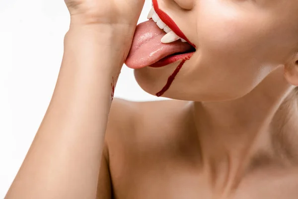 Cropped shot of naked girl with vampire teeth licking blood from hand isolated on white — Stock Photo