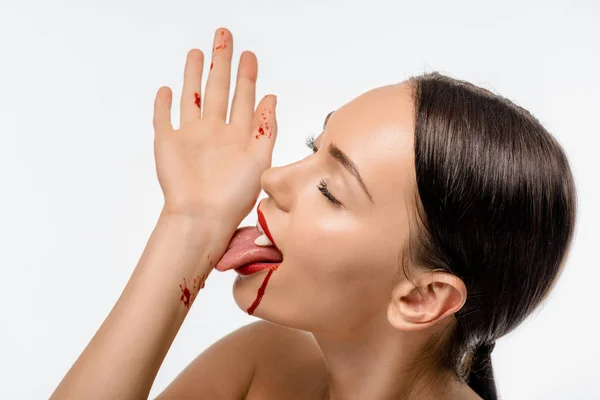 Naked girl with vampire teeth licking blood from hand isolated on white — Stock Photo