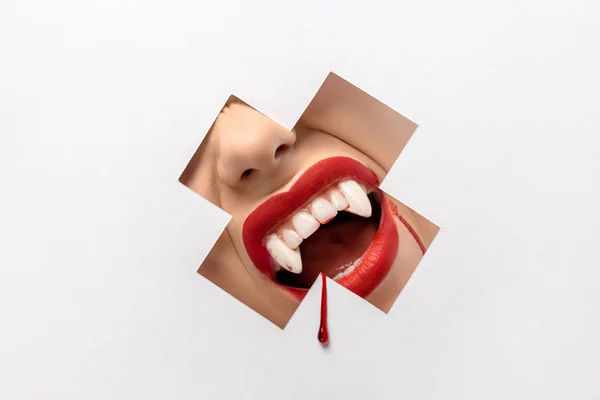 Cropped shot of woman showing vampire teeth through cross shaped hole on white — Stock Photo