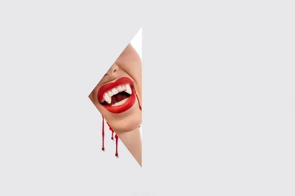 Abgeschnittene Aufnahme einer Frau, die Vampirzähne durch ein Loch auf Weiß zeigt — Stockfoto