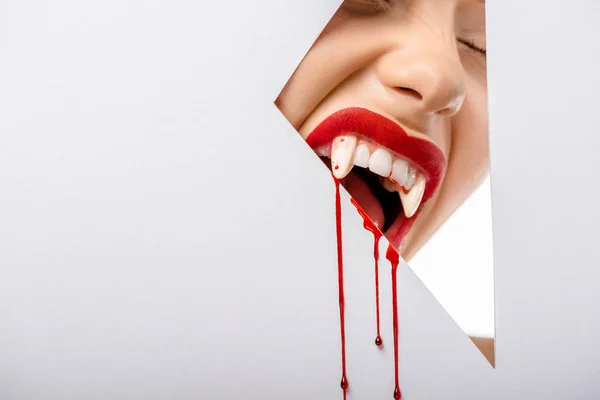 Cropped shot of girl with vampire teeth and blood biting through hole on white — Stock Photo