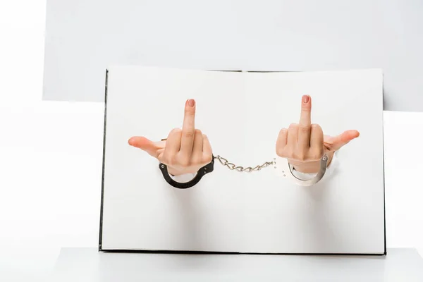 Cropped shot of female hand in handcuffs showing middle fingers through holes on white — Stock Photo