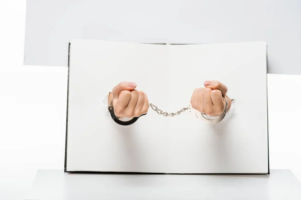 Cropped shot of female hand in handcuffs through holes on white — Stock Photo