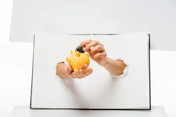 Cropped shot of woman putting bitcoin into yellow piggy bank through holes on white — Stock Photo