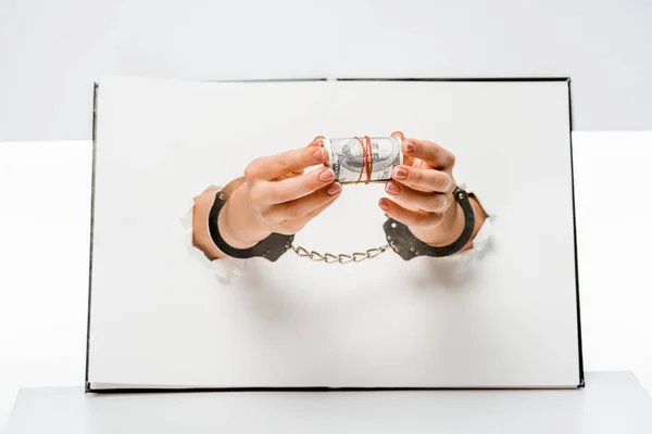 Cropped shot of woman in handcuffs holding dollar banknotes through holes on white — Stock Photo