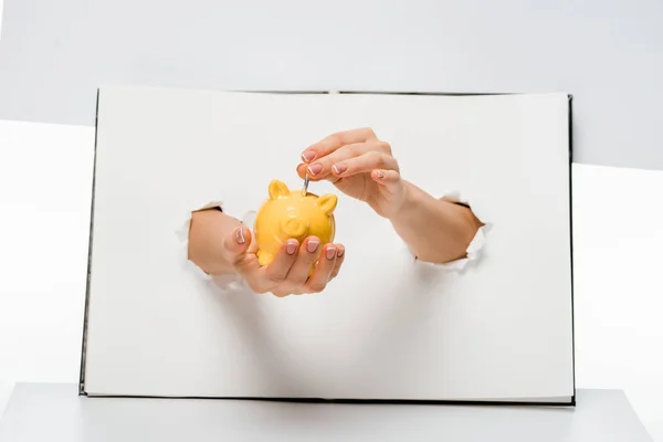 Cropped shot of woman putting coin into yellow piggy bank through holes on white — Stock Photo