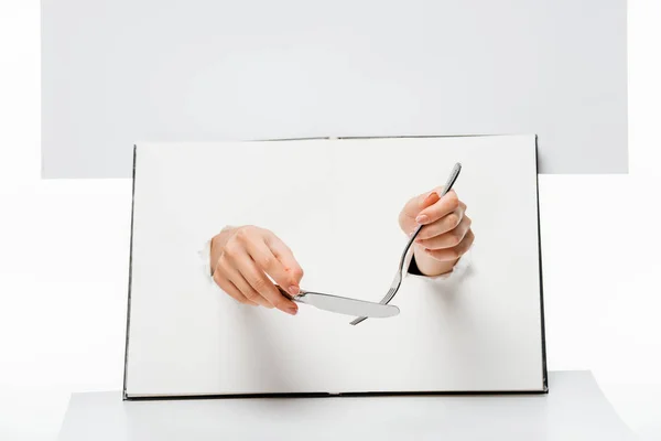 Recortado tiro de mujer sosteniendo tenedor y cuchillo a través de agujeros en blanco - foto de stock